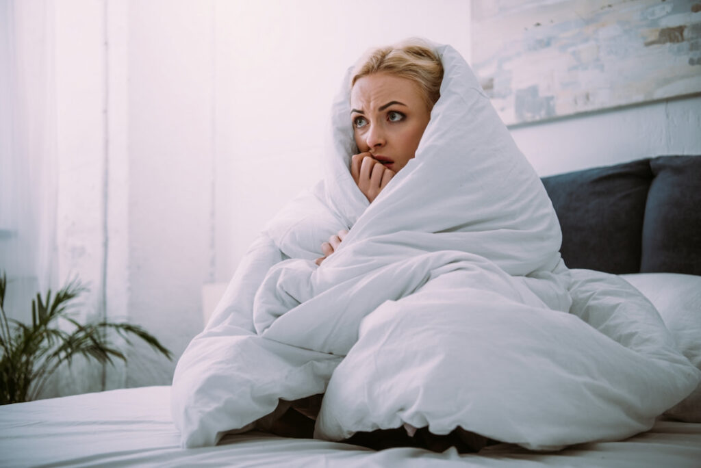 a scared woman in bed covered with blanket