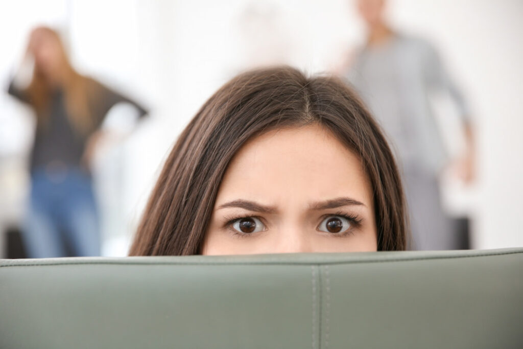 a frightened woman hiding behind the sofa