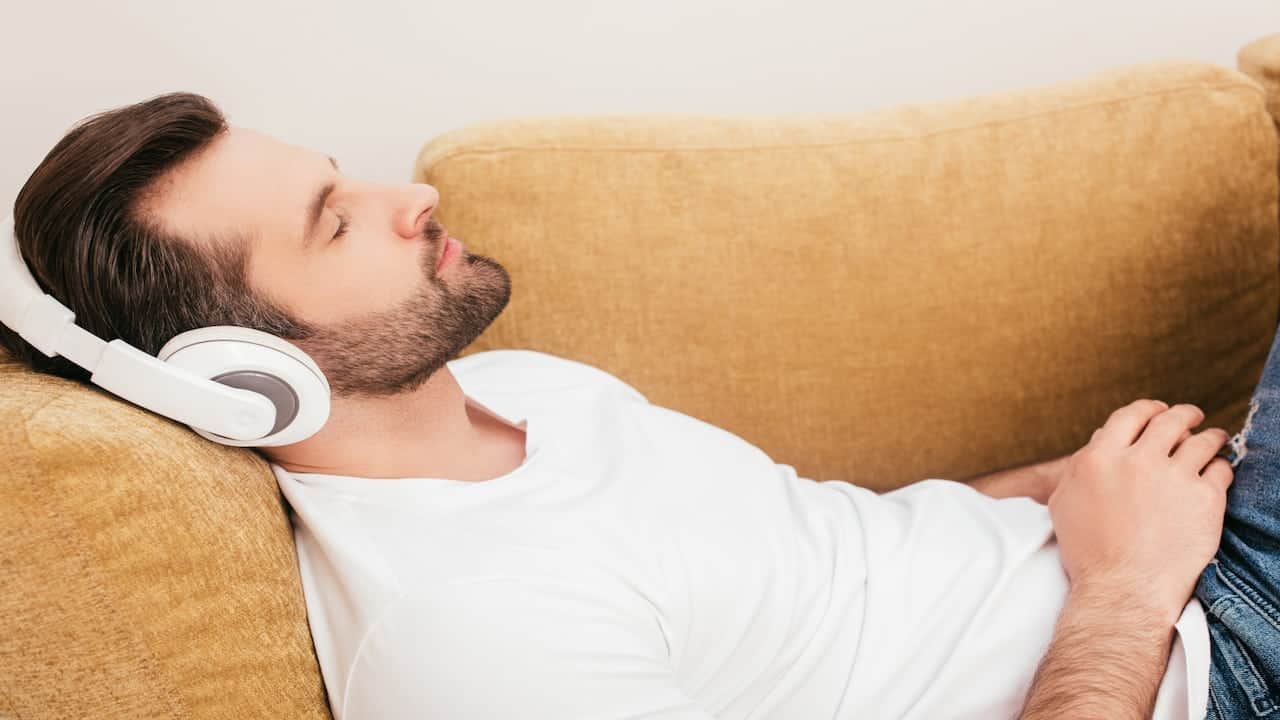 A man lying on the couch with headphones on his head