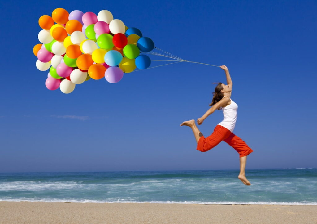 a young woman holding balloons and jumping by the sea