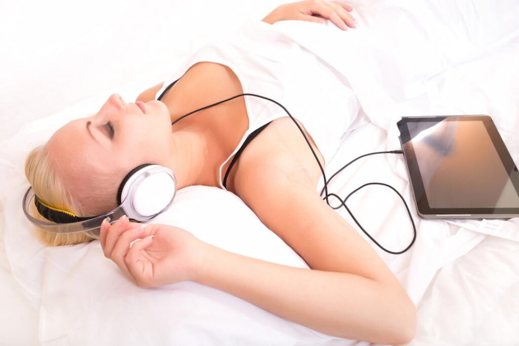 a blonde woman lying in the bed with tablet and headphones 