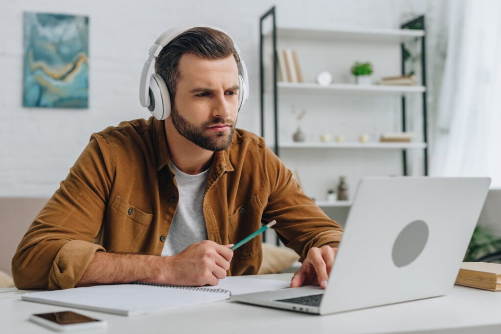 a man with headphones looking at his laptop and making notes