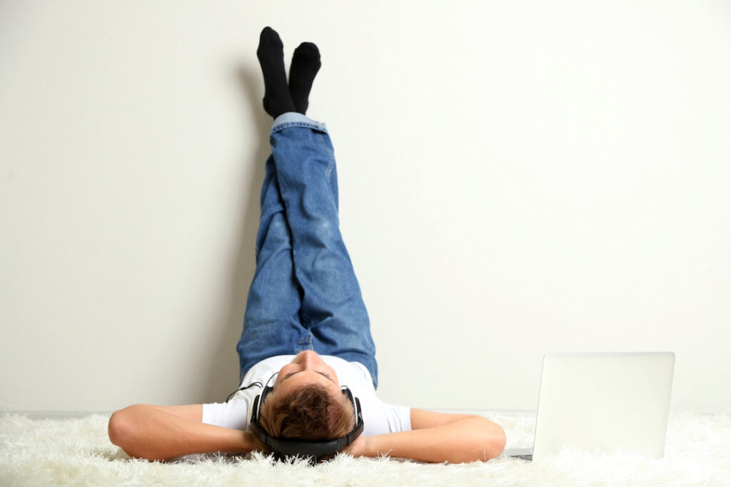 a man lying down on the floor with his legs up against the wall and headphones on his head