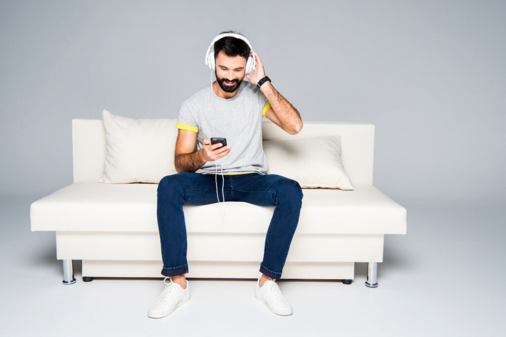 young bearded man with white headphones on his head sitting on the couch