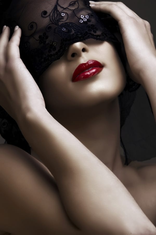 portrait of woman wearing red lipstick and black mask over her eyes