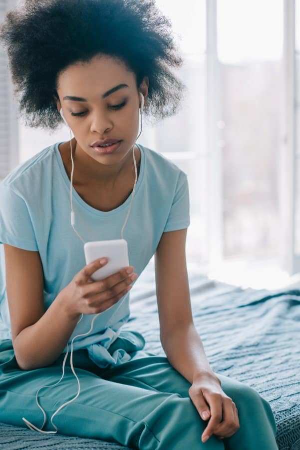 a girl with earbuds sitting on the bed