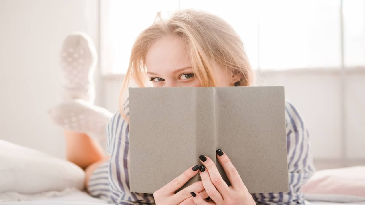 a blonde woman hiding her face behind an opened book