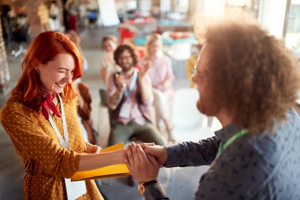 a young woman blushing while shaking hands with her colleague 