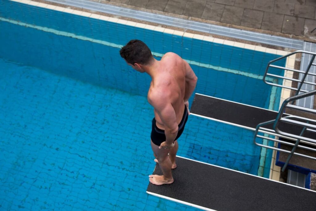 man standing on diving board and looking down to the pool water  