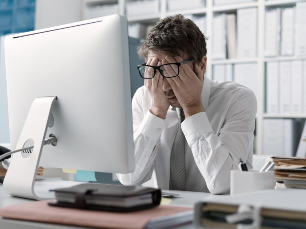 a man at his working desk rubbing his eyes