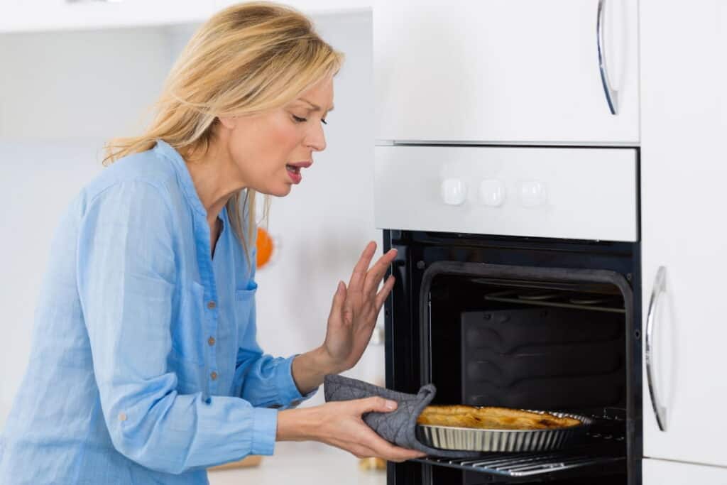 a woman taking out a hot pie from the oven 