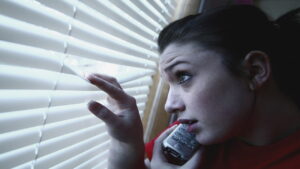 a girl on the phone, peeking out a window