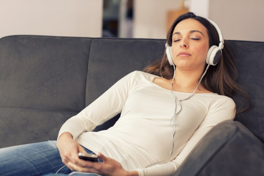 a woman with headphones listening to the audios on the couch