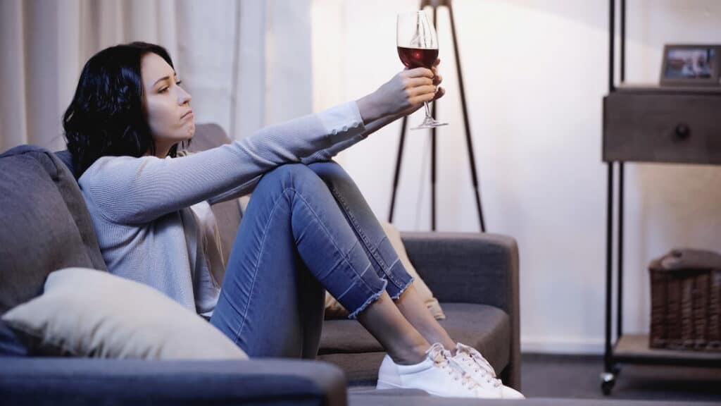 a sad woman sitting on the sofa with a glass of wine in her hands