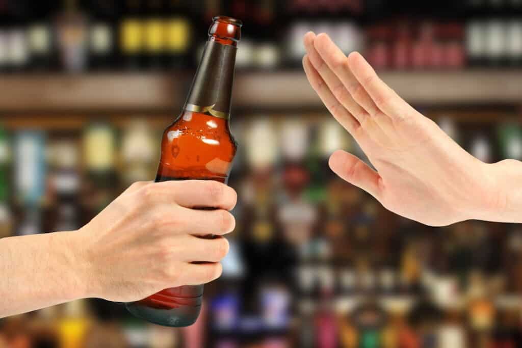 a hand gesture showing no to the bottle of beer
