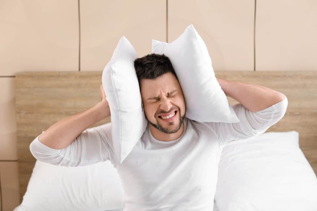 a man covering his ears with pillows