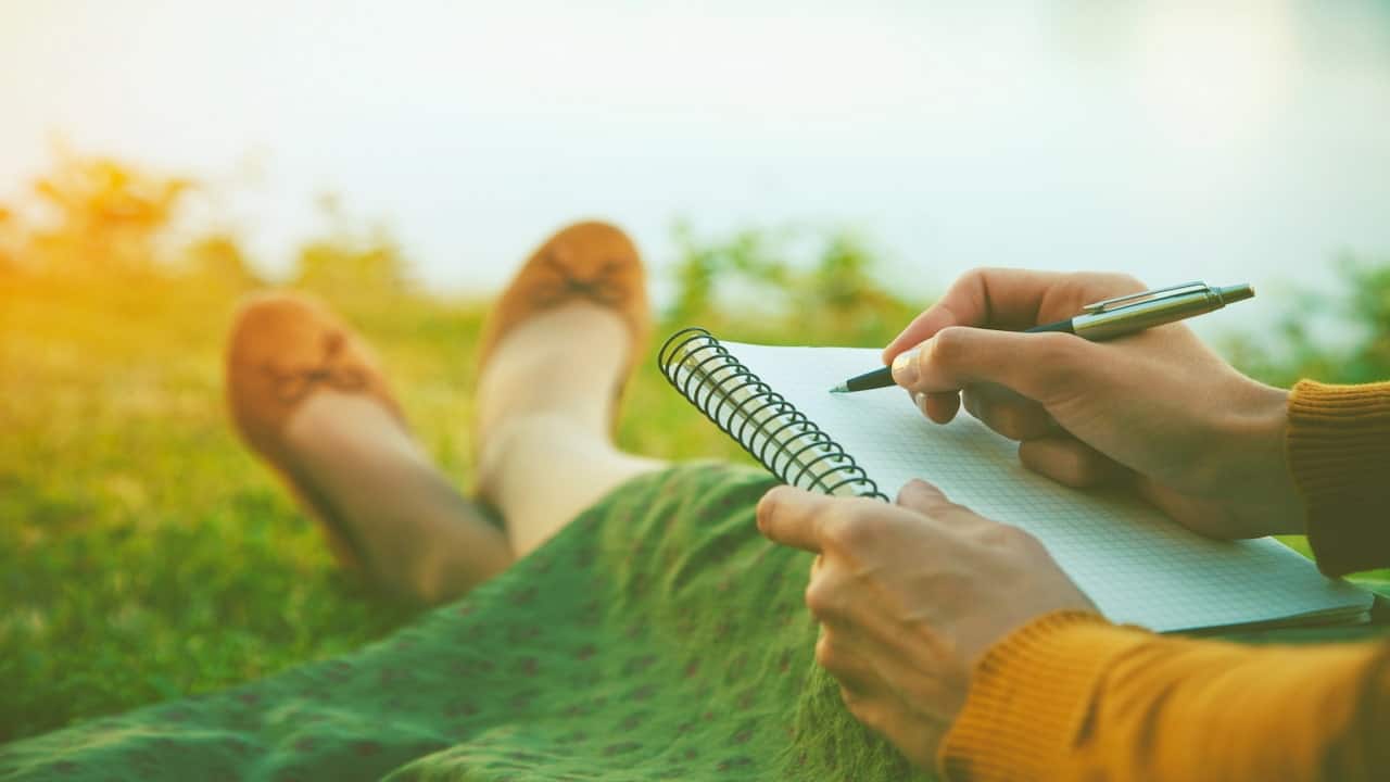 a woman sitting on the grass with a notebook and a pen