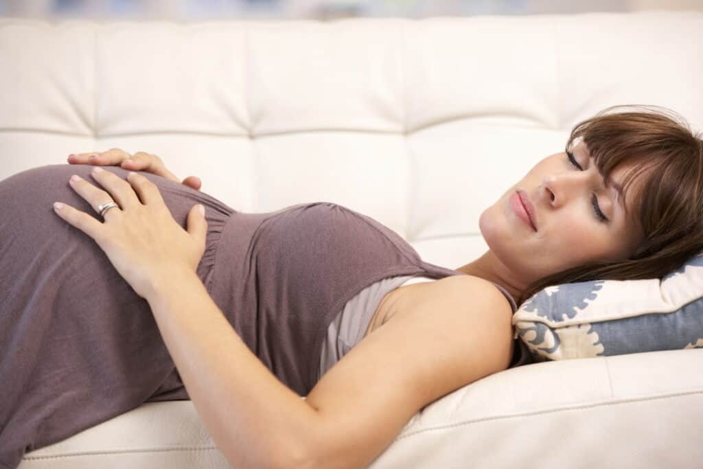 a pregnant woman lying on the couch with her eyes closed