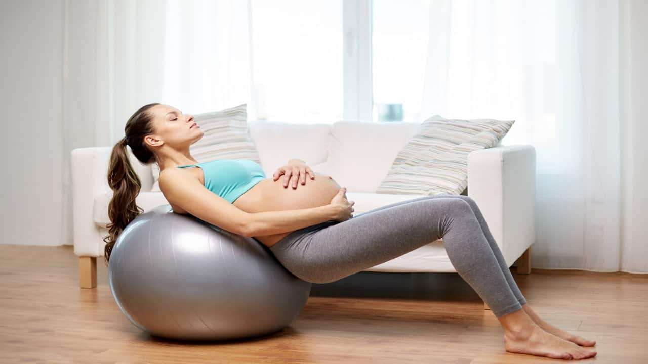 a pregnant woman resting on a fitness ball