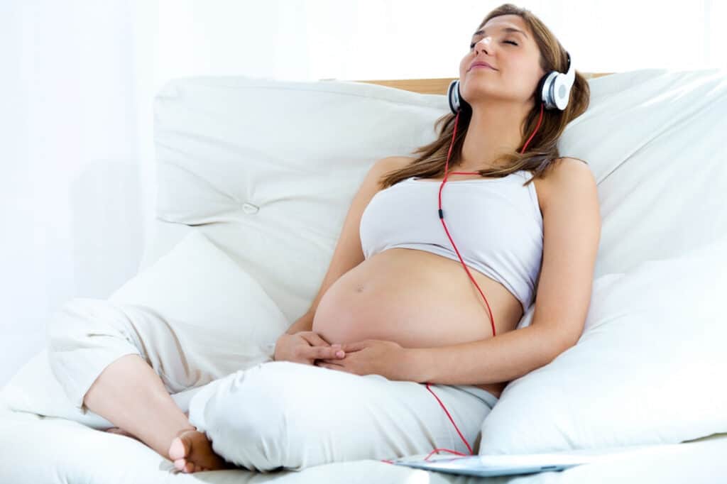 pregnant woman relaxing n the pillows while listening to audios