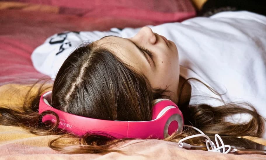 a young woman lying on the bed and listening to audio downloads