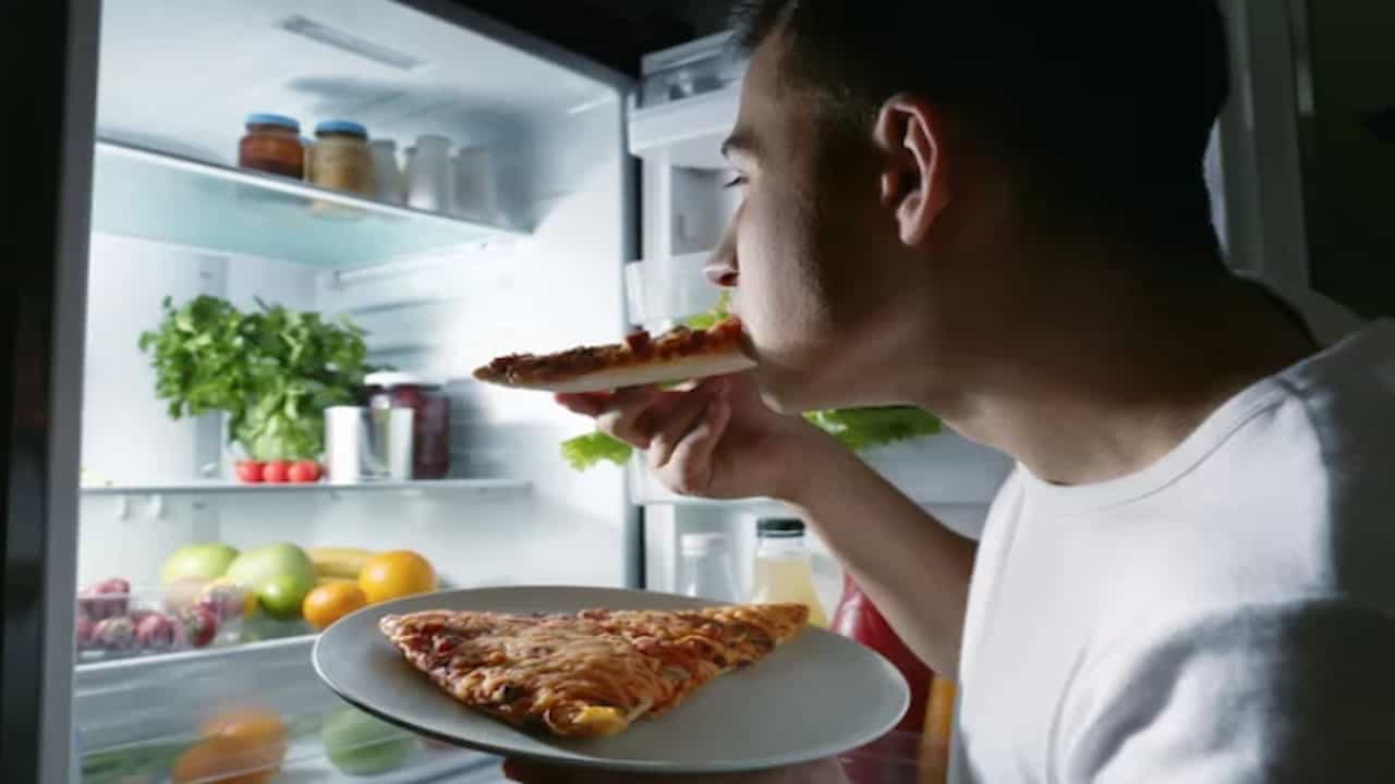 a man eating pizza in front of the fridge