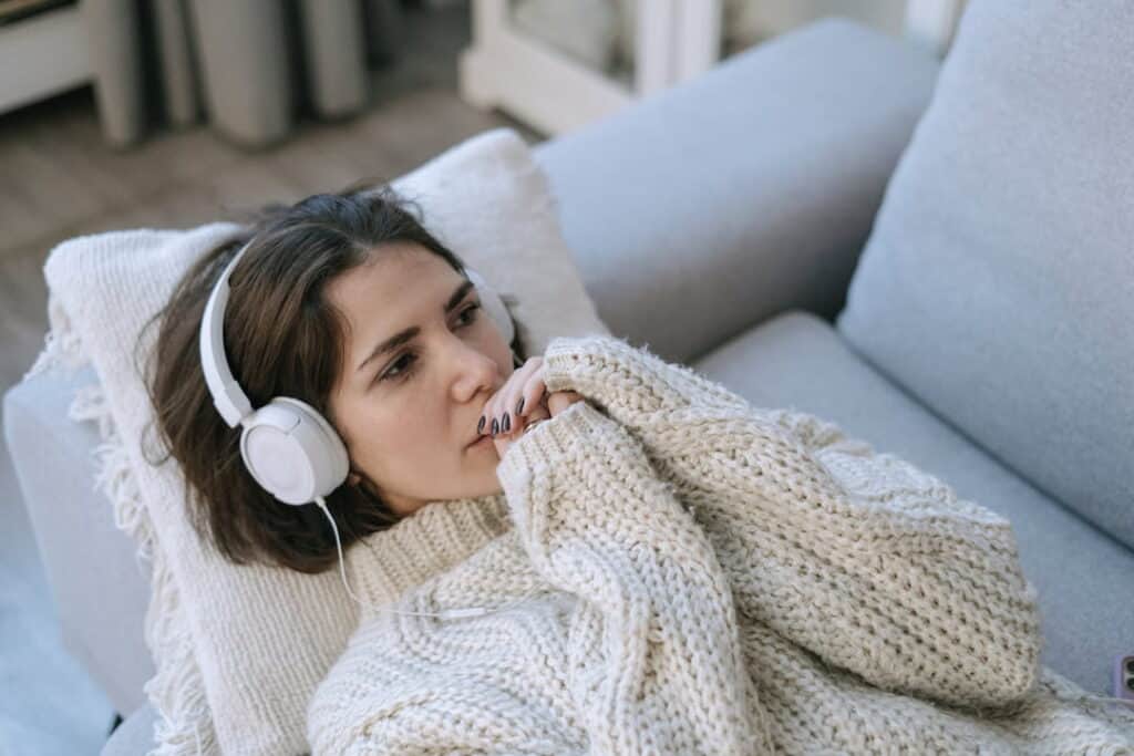 a woman lying down on the couch and listening to audio downloads